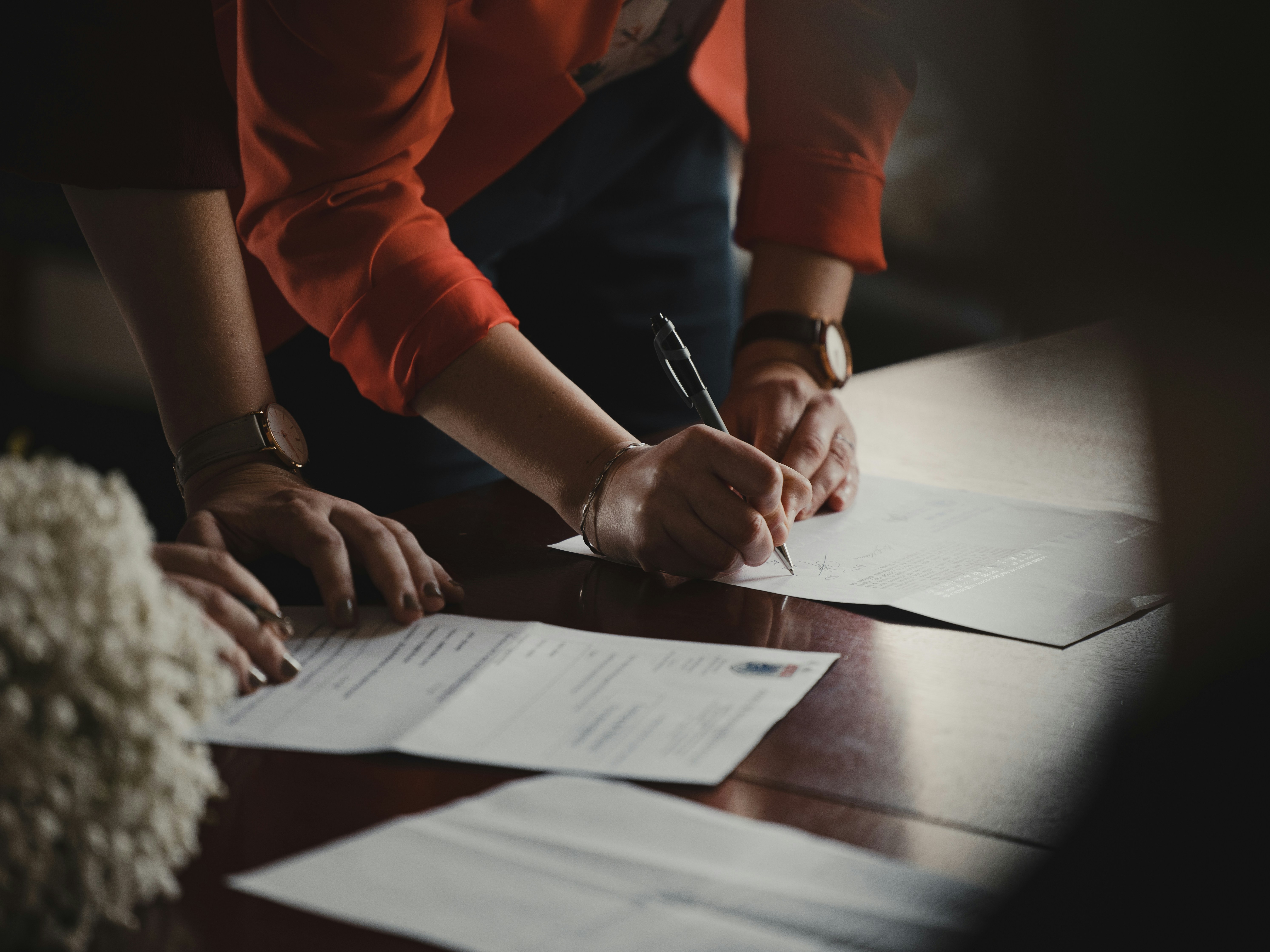 A person signing a paper with another person overlooking